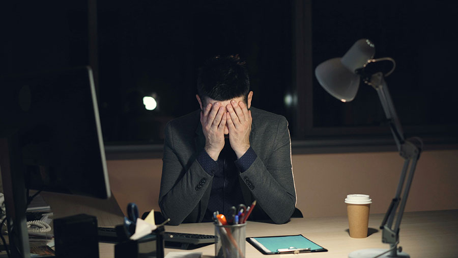 Un homme &agrave; son bureau, les mains sur le visage.