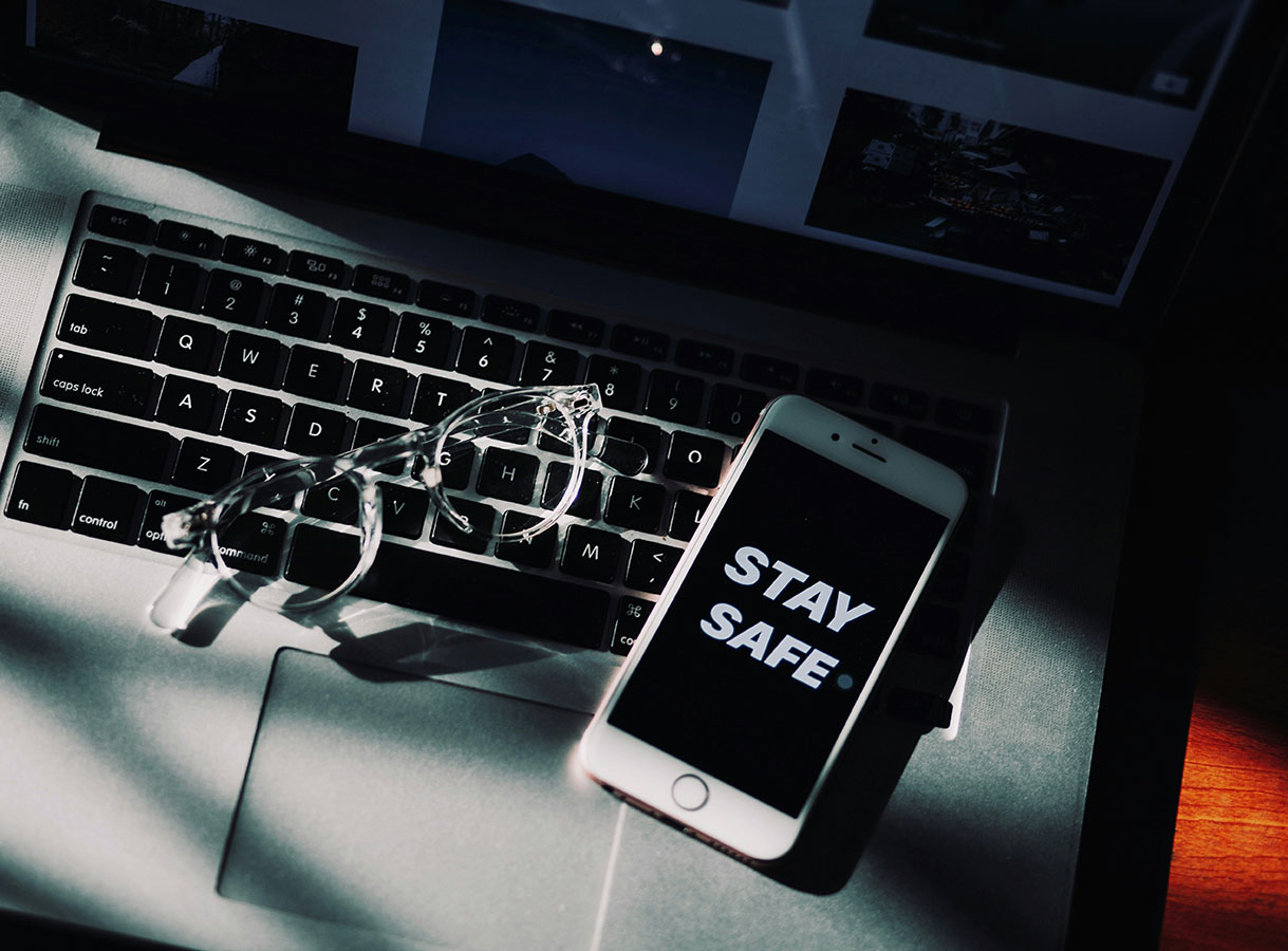 Un ordinateur avec une paire de lunettes et un t&eacute;l&eacute;phone sur lequel est inscrit &laquo; Stay safe &raquo;