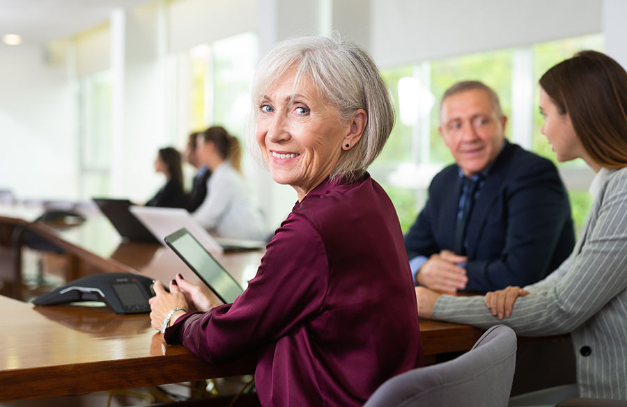 Portrait de côté d'une femme d'affaires blanche aux cheveux gris, souriante et amicale, assise à une table lors d'une réunion d'équipe d'entreprise dans une salle de conférence